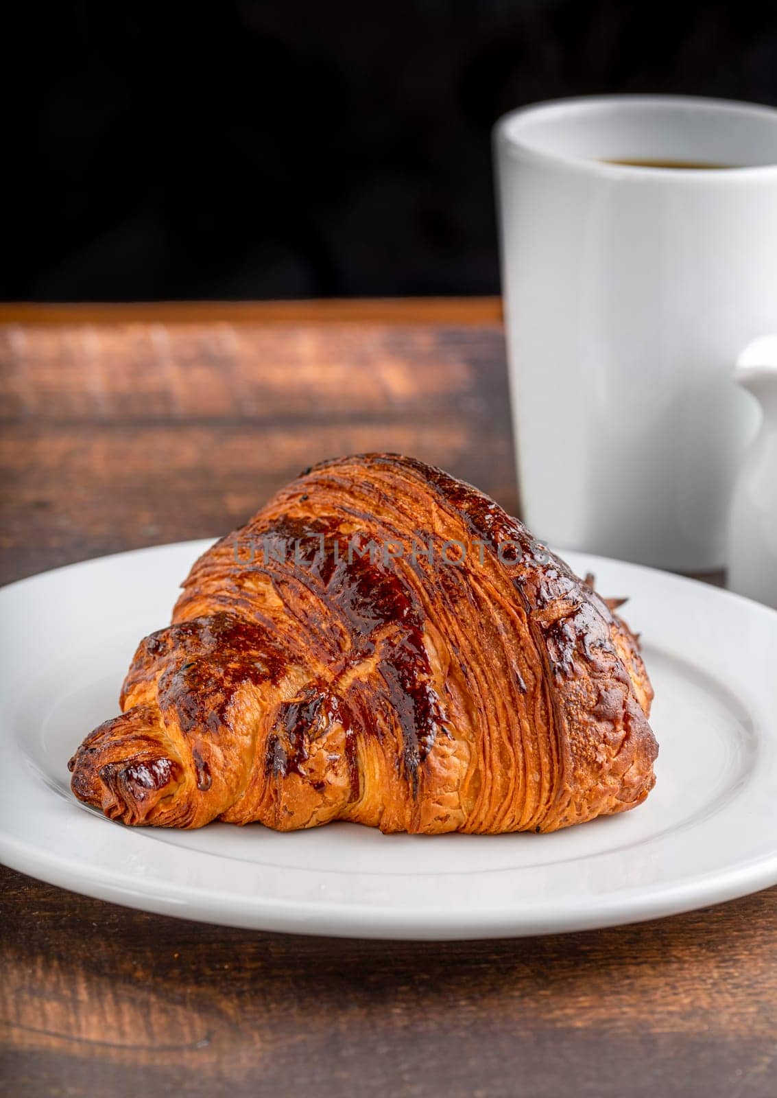 Croissant with coffee next to it on wooden table