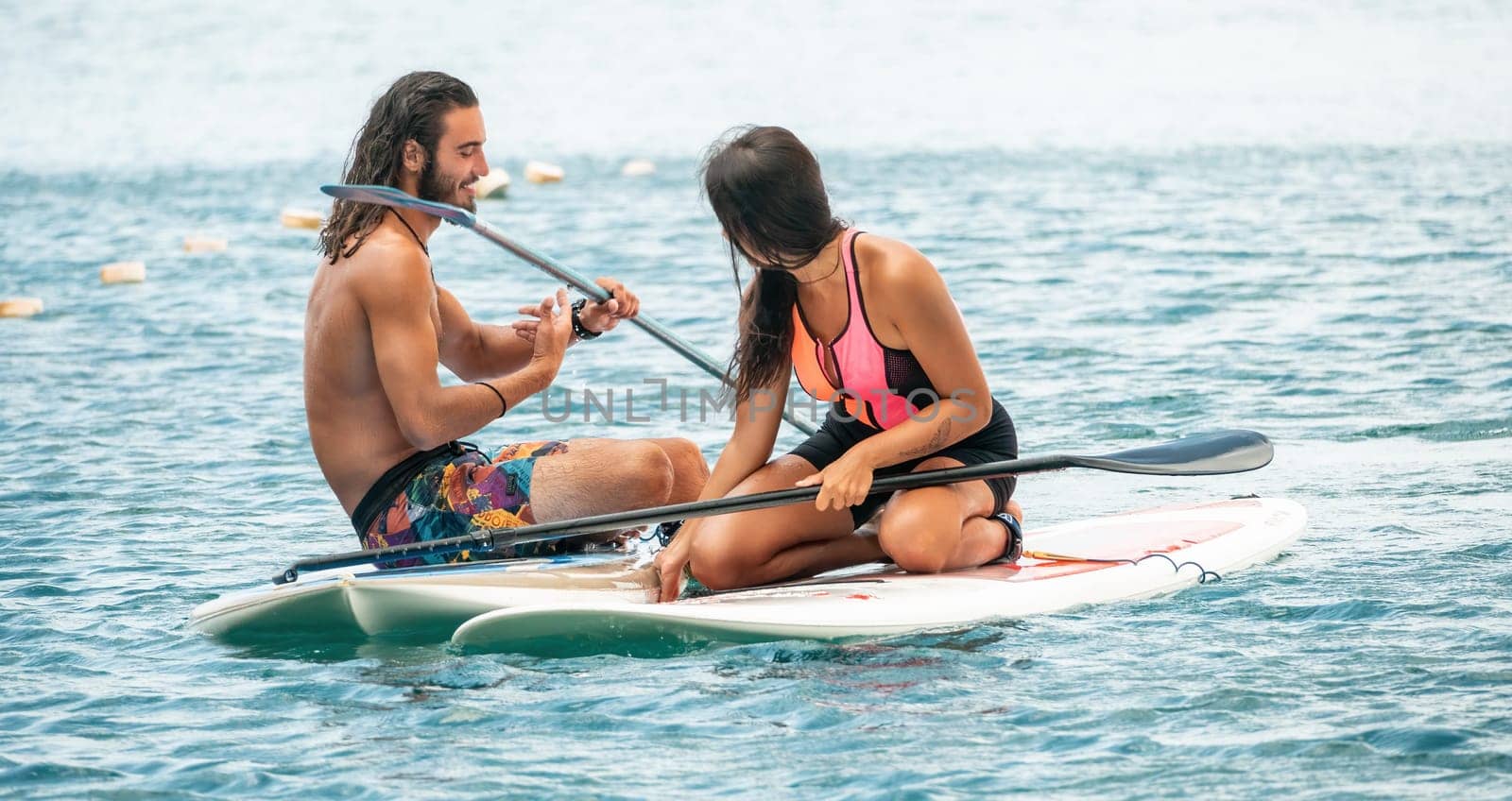 Sea woman and man on sup. Silhouette of happy young woman and man, surfing on SUP board, confident paddling through water surface. Idyllic sunset. Active lifestyle at sea or river