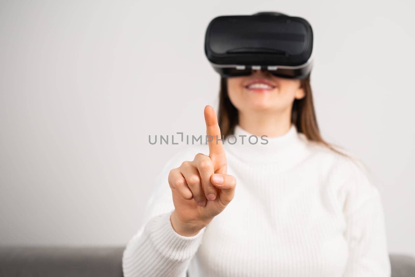 Smiling woman touching air with a finger in VR glasses. Metaverse technology concept.