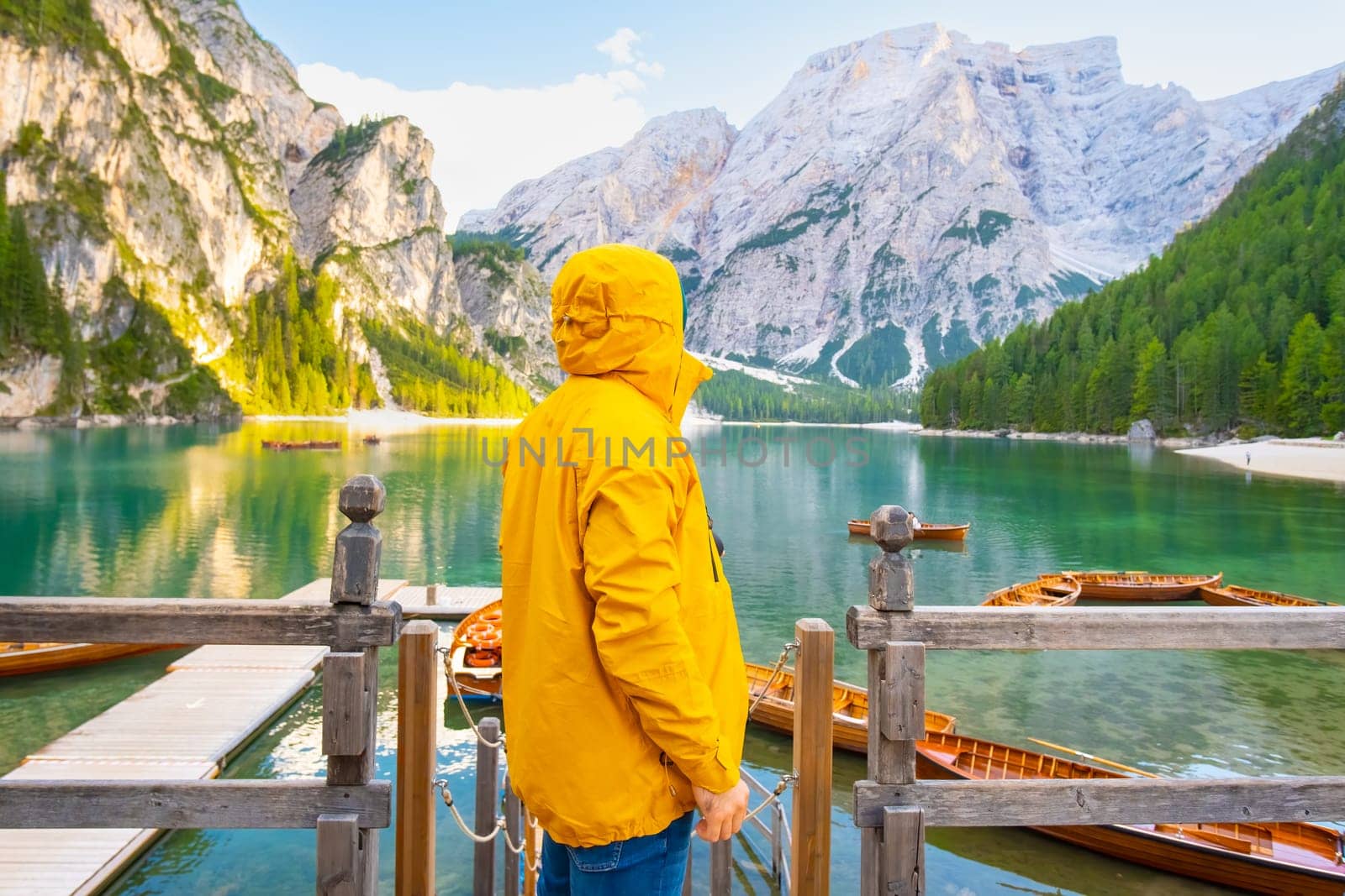 Tourist with hiking outfit enjoying the amazing view of alpine lake Braies with boats and Dolomites. Man in a yellow sport jacket looking into the distance