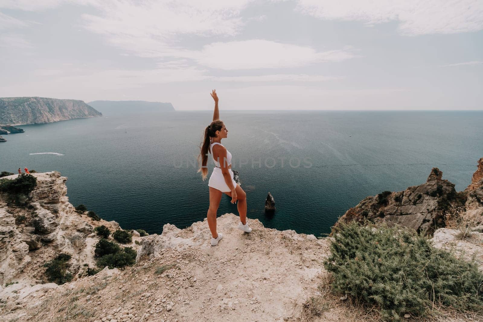 Woman travel sea. Happy tourist in hat enjoy taking picture outdoors for memories. Woman traveler posing on the beach at sea surrounded by volcanic mountains, sharing travel adventure journey