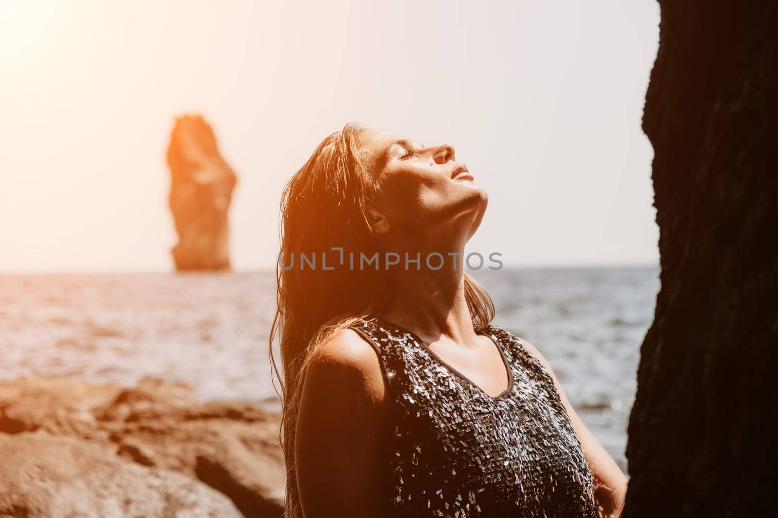 Woman travel sea. Young Happy woman in a long red dress posing on a beach near the sea on background of volcanic rocks, like in Iceland, sharing travel adventure journey