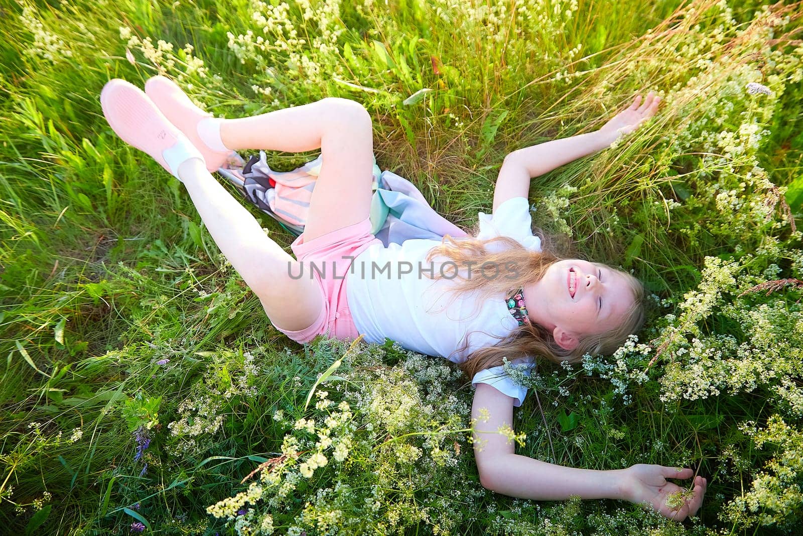 Pretty blonde girl having fun in a meadow on a natural landscape with grass and flowers on a sunny summer day. Portrait of a teenage child in summer or spring outdoors on field