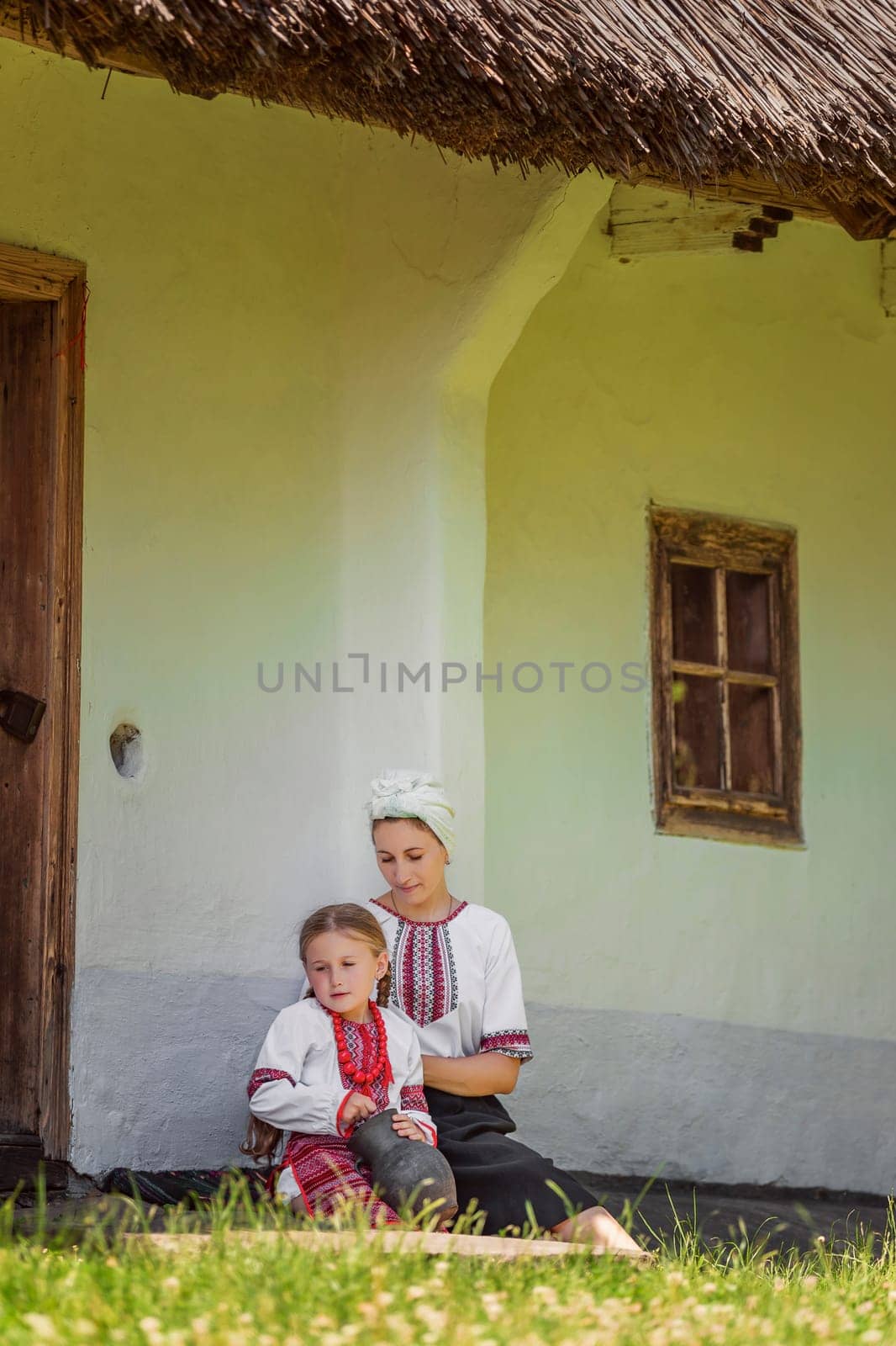 mother and daughter in traditional Ukrainian clothes are sitting near the house