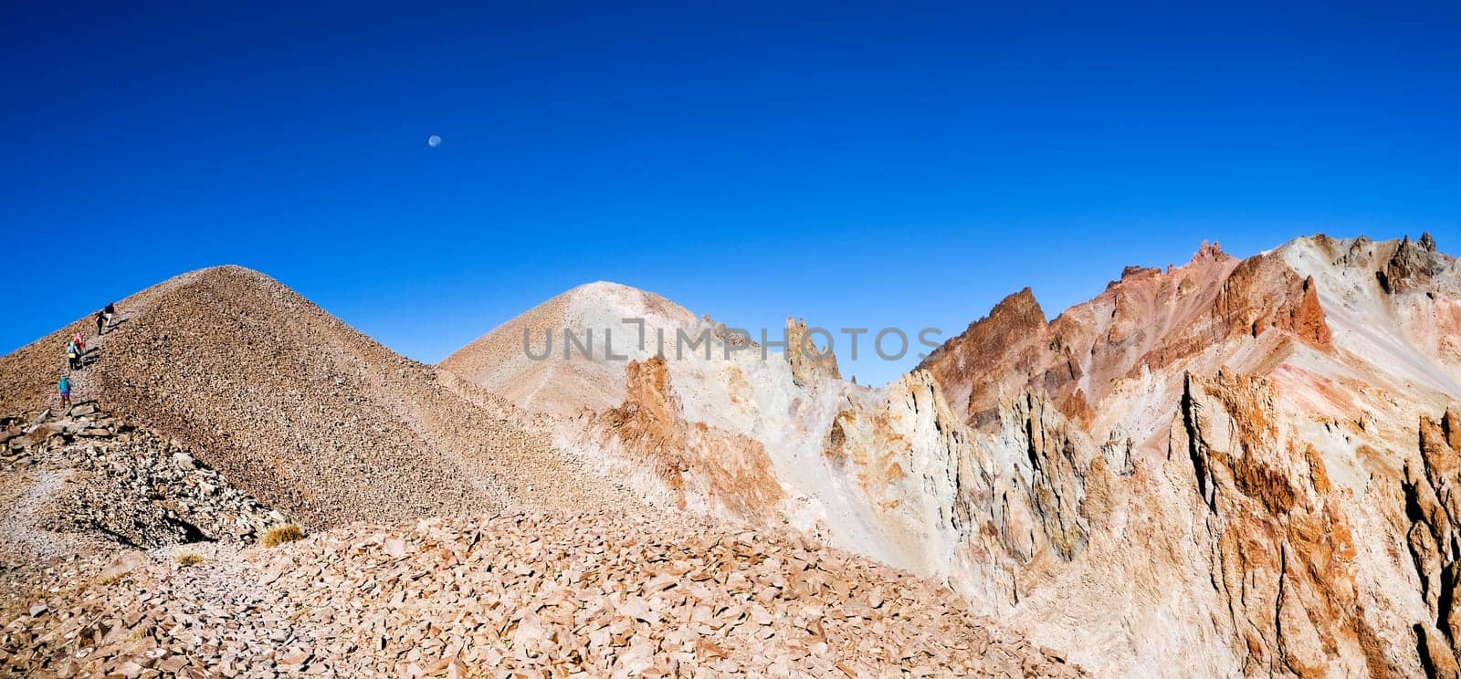 Panoramic view of stony mountains with tourists on blue sky background