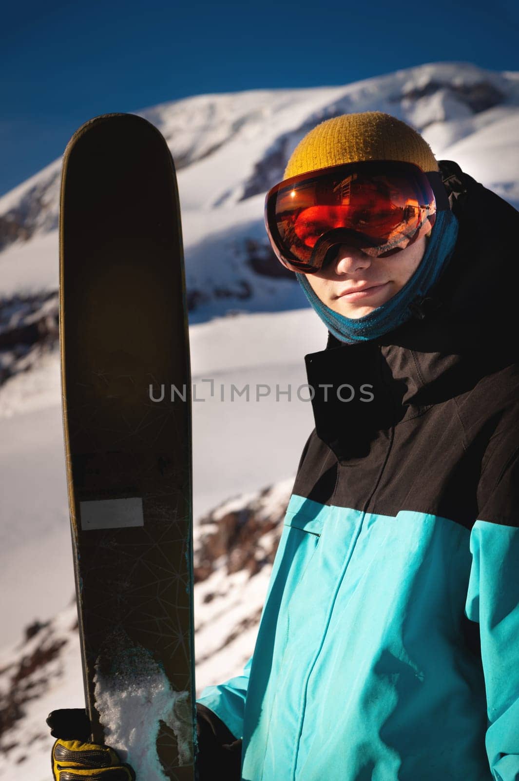 Happy man standing with skis in front of the mountains on a sunny day. Young man smiling looking at camera and holding skis, portrait of satisfied tourist in ski resort by yanik88