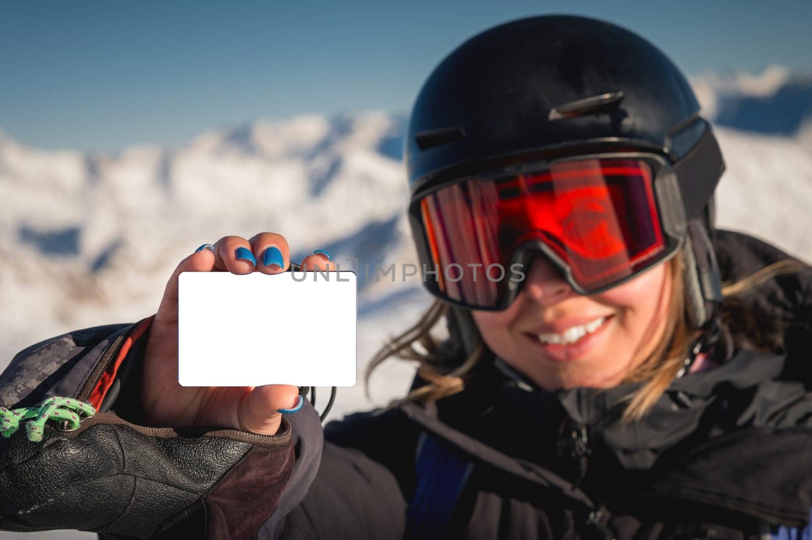Winter sports girl holding a ski pass and smiling. A concept illustrating the entry fee for skiing. Happy woman showing blank lift pass.