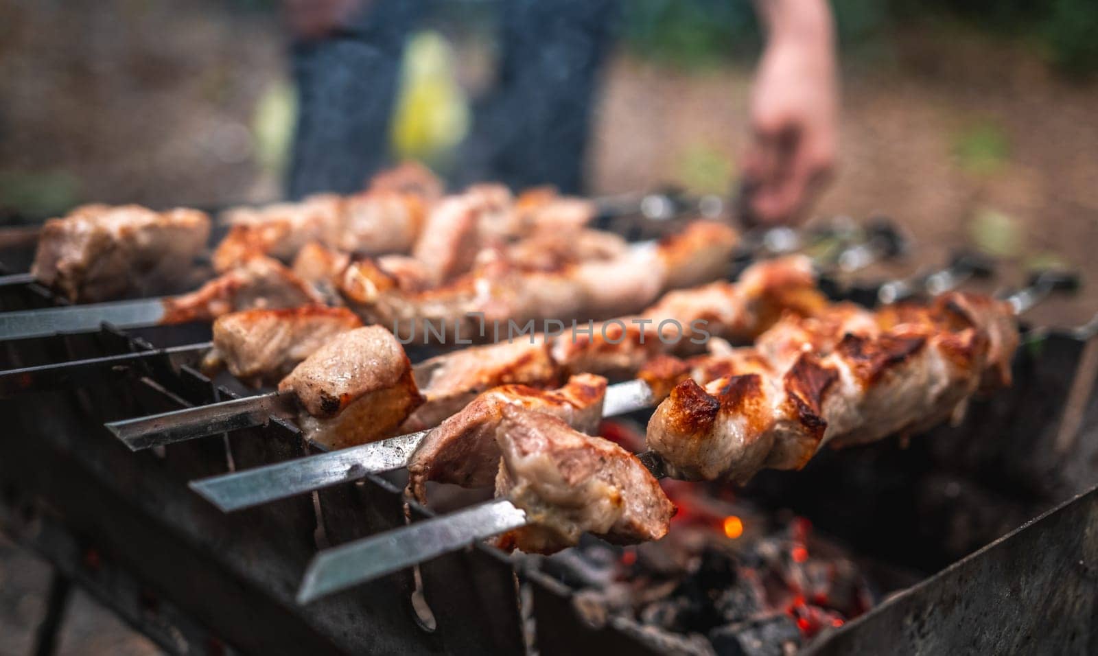 Man hand straightens the metal skewer with barbecue delicious grilled meat with smoke on brazier outdoors. Person preparing pork steaks on fired charcoals. Hot BBQ closeup