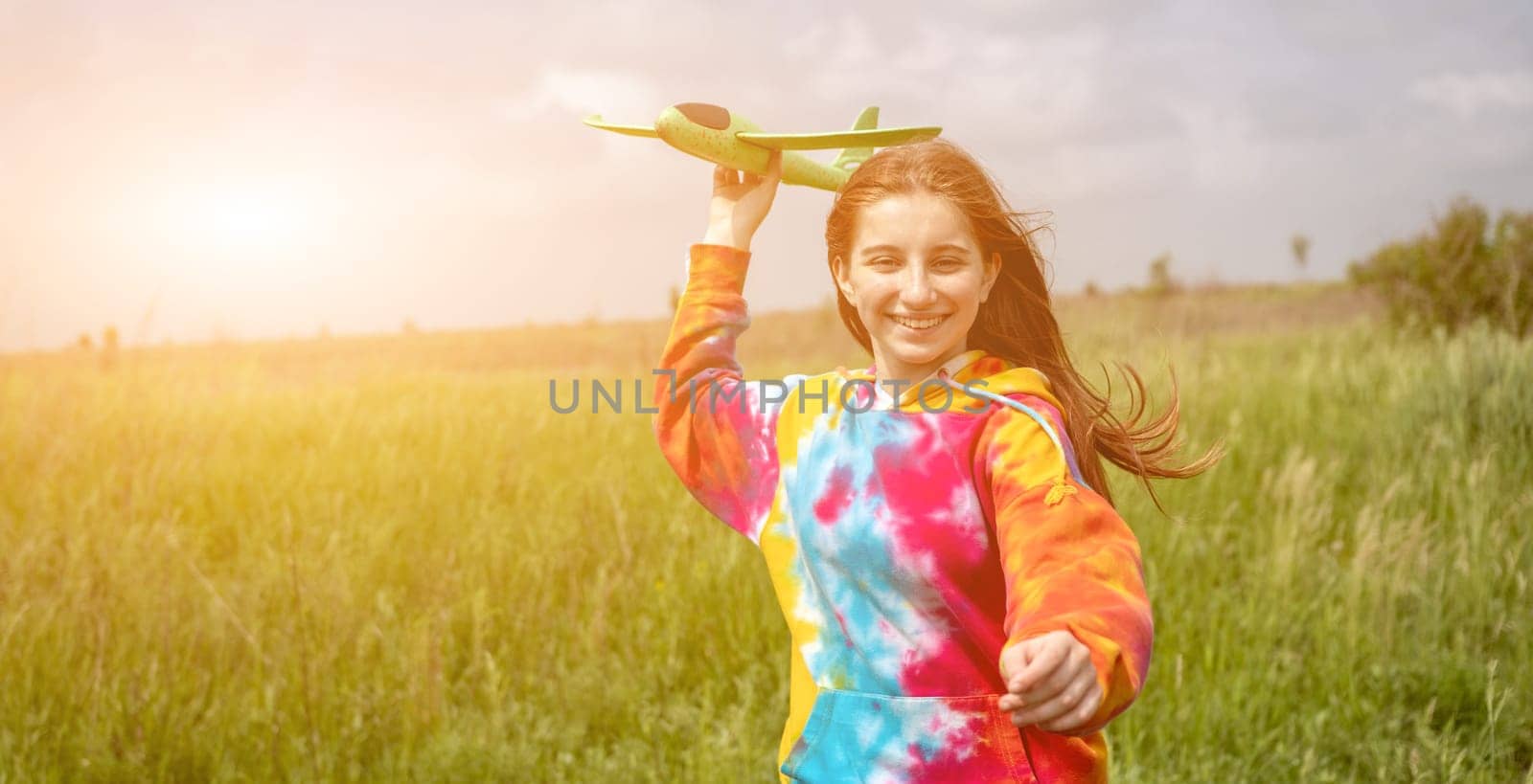 Portrait of beautiful girl playing with toy plane outdoors in the field in sunny rays. Teenager female person launching airplane at the nature. Concept of freedom and hobby