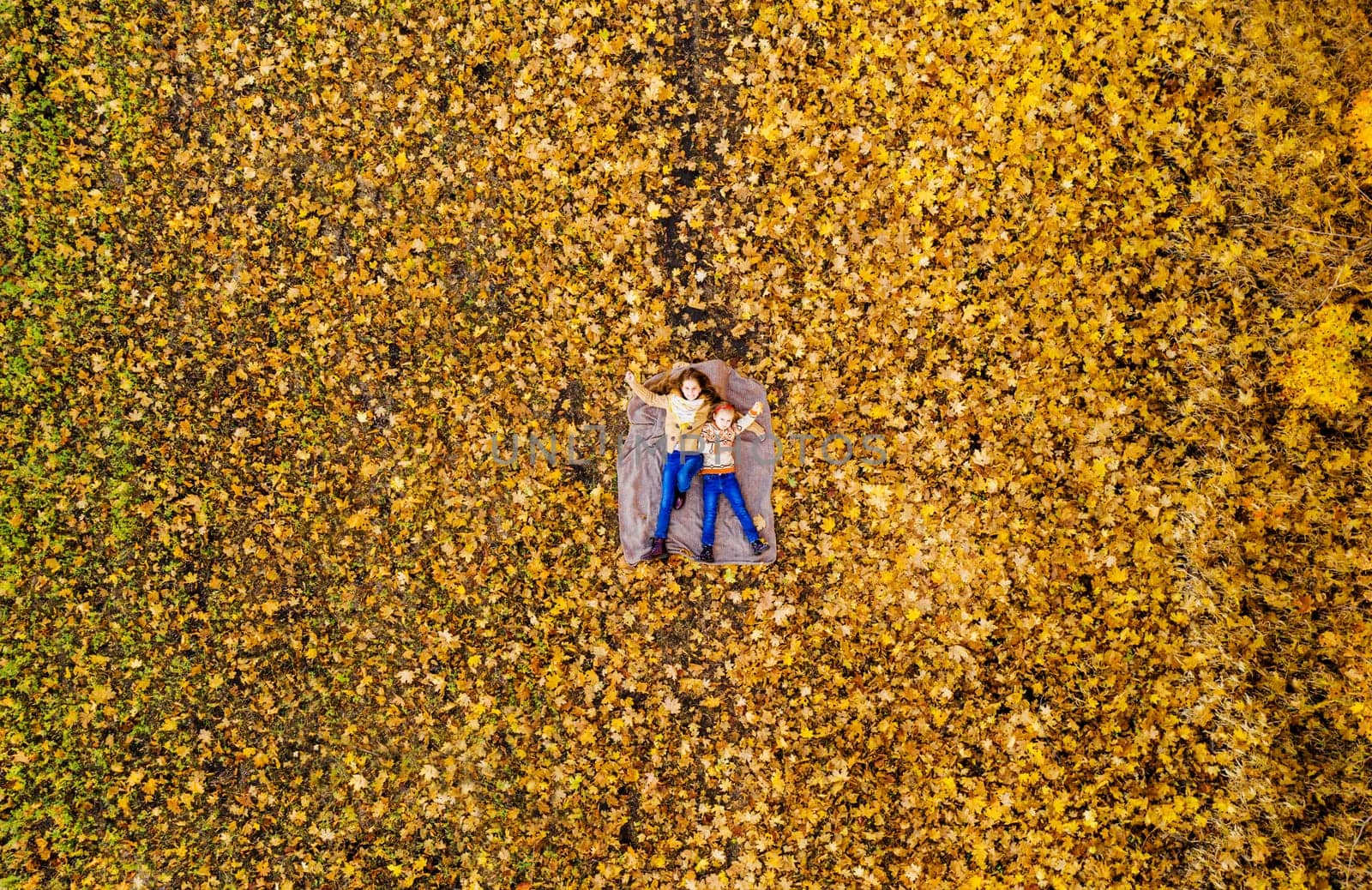 Top view on sisters lying on yellow leaves in park