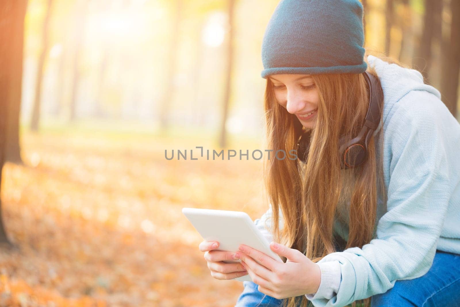 Smiling girl reading on tablet sitting in park