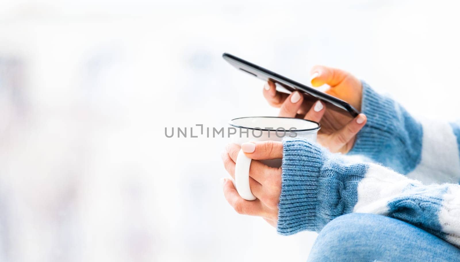 Cup and smartphone in female hands close up