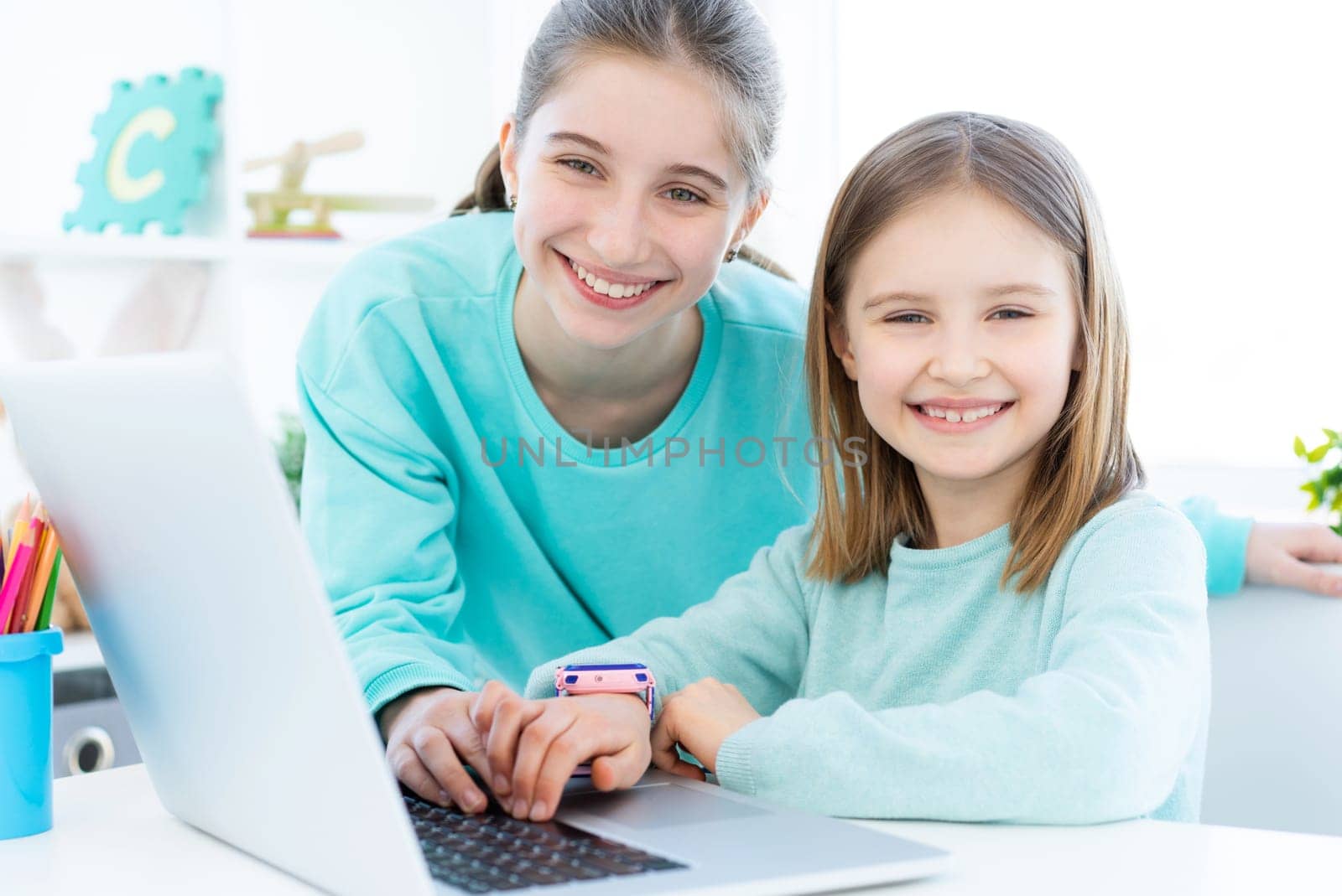 Smiling sisters next to modern laptop in light room