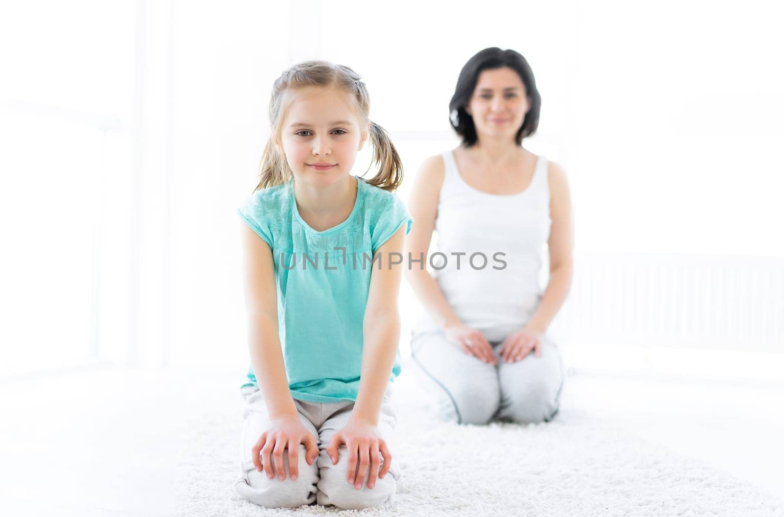 Cute little girl doing fitness with mother in bright room