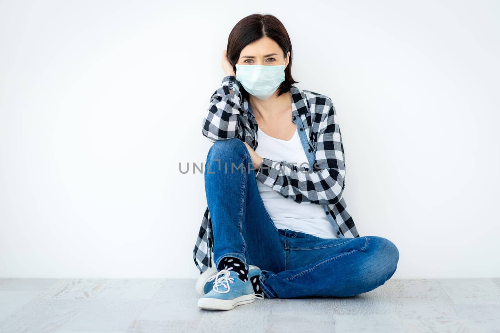 Attractive woman in medical mask sitting on floor indoors