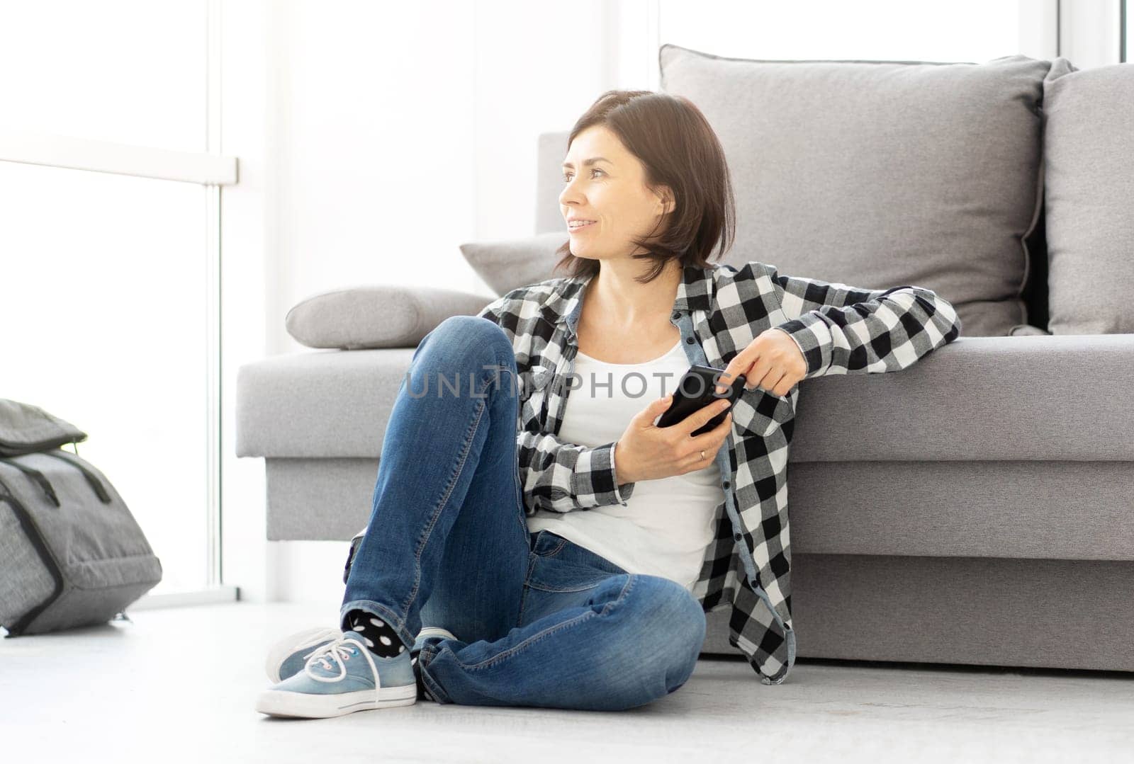 Pretty woman with smart phone sitting on floor in modern apartment