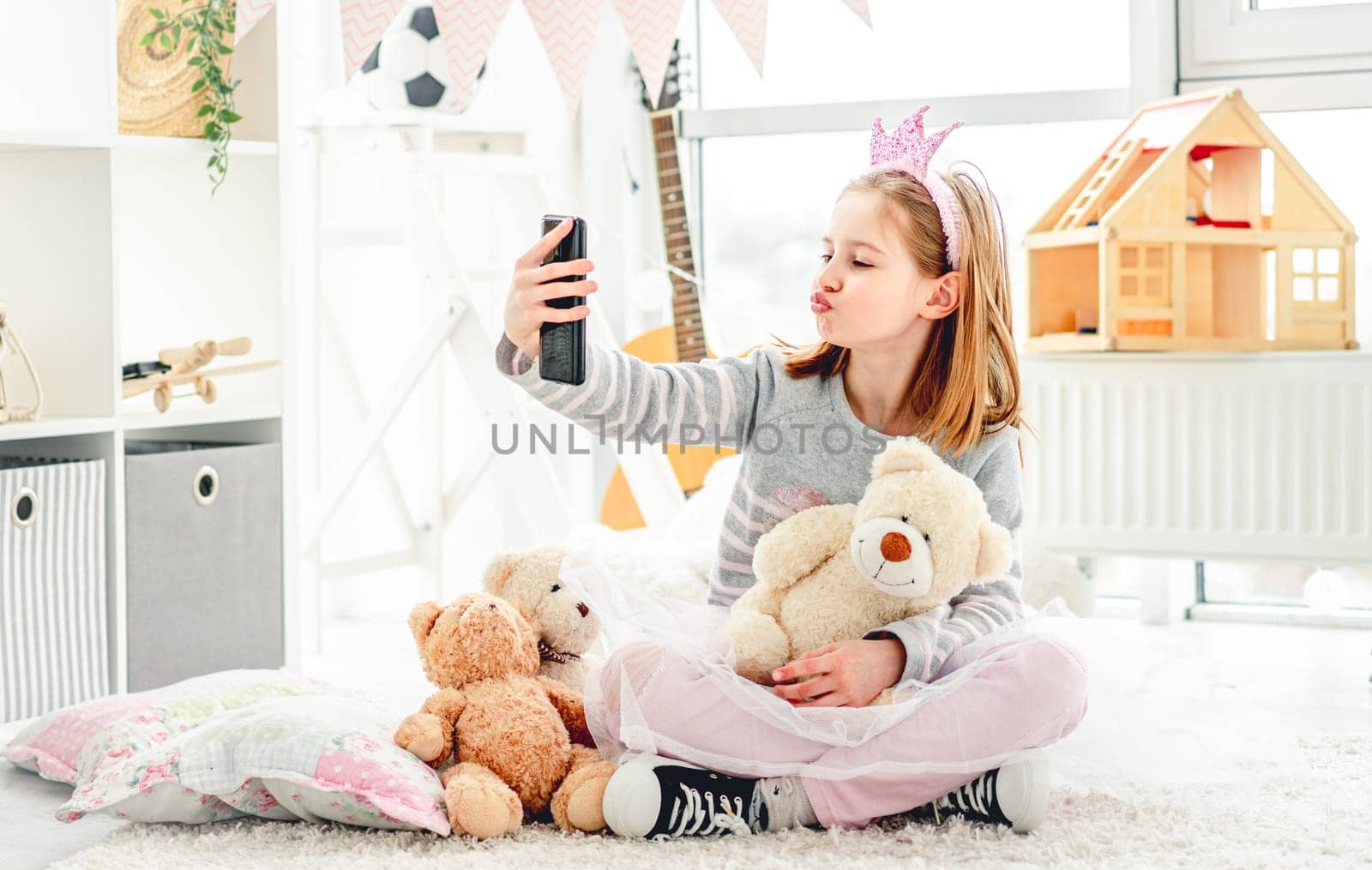 Funny little girl with teddy bear taking selfie in cozy room