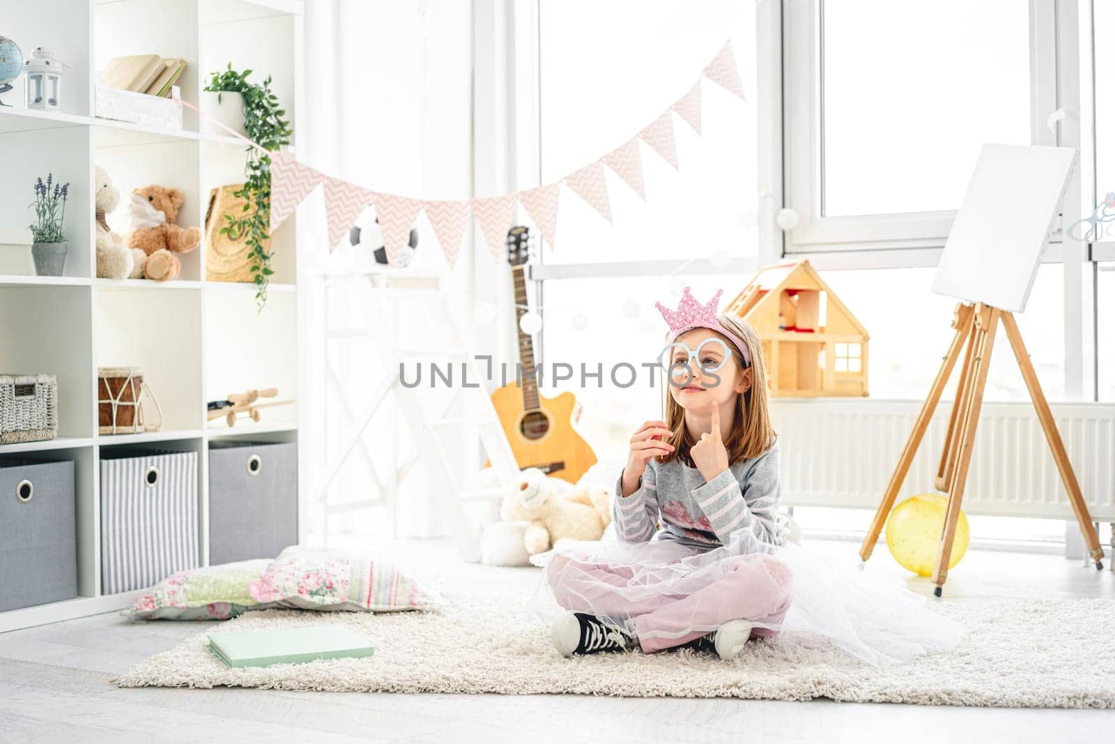 Pretty little girl playing with paper glasses in bright room