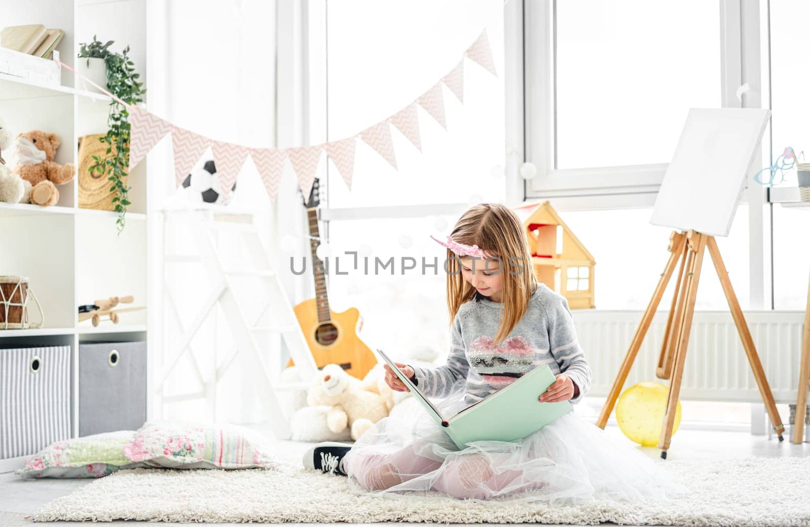 Beautiful little girl reading intersting book sitting on floor in children room