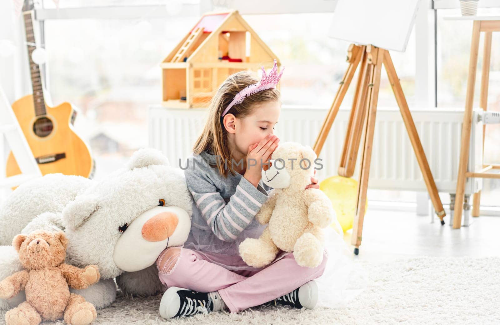 Happy little girl sharing secrets with teddy bear in light room