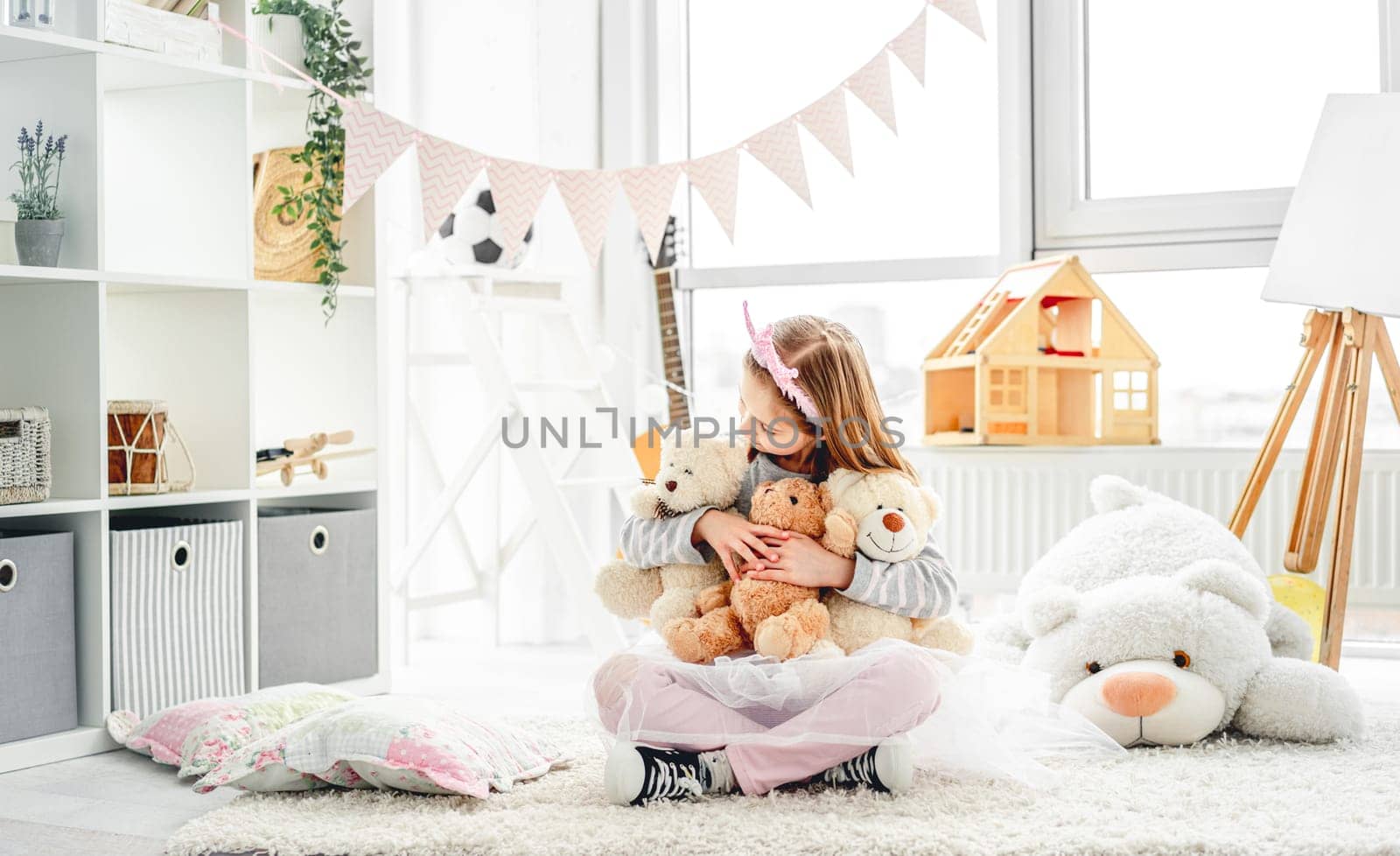 Smiling little girl hugging teddy bears sitting on floor indoors