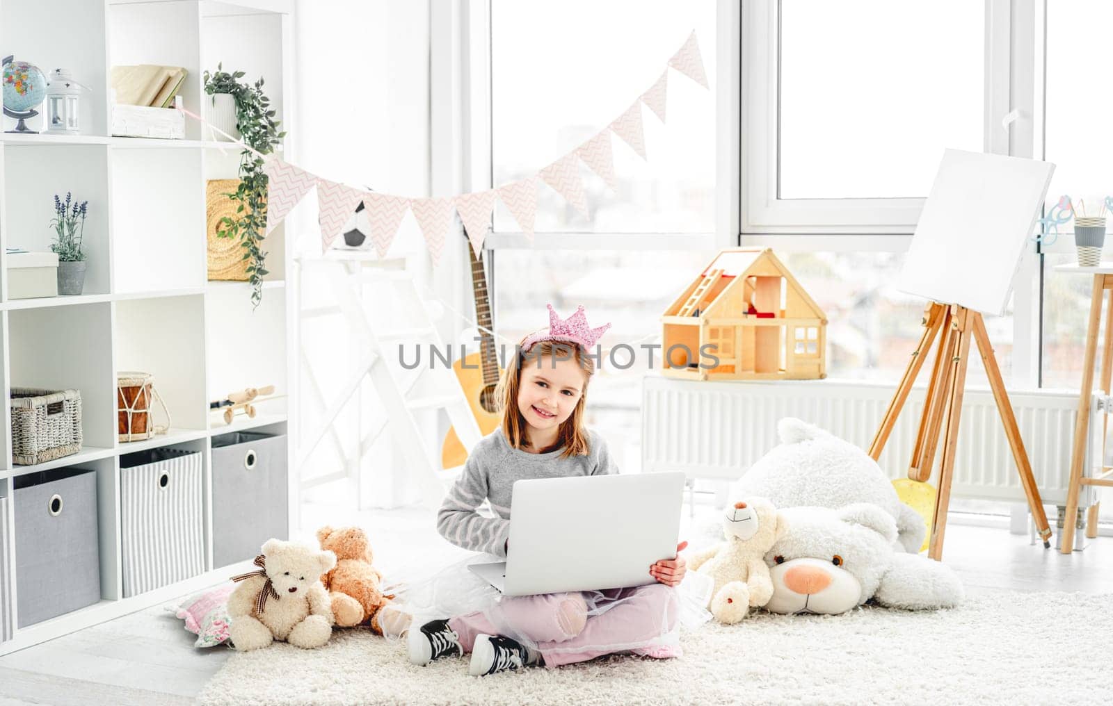 Cute little girl sitting on floor with laptop in playroom