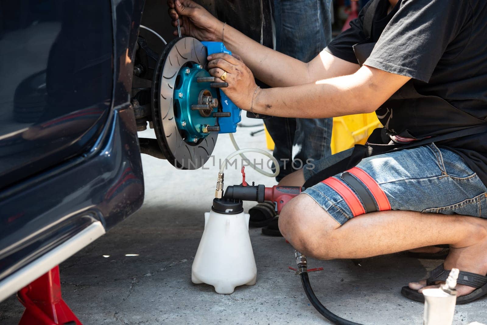 Bangkok, Thailand - March 6, 2021 : Unidentified car mechanic or serviceman disassembly and checking a disc brake and asbestos brake pads for fix and repair problem at car garage or repair shop