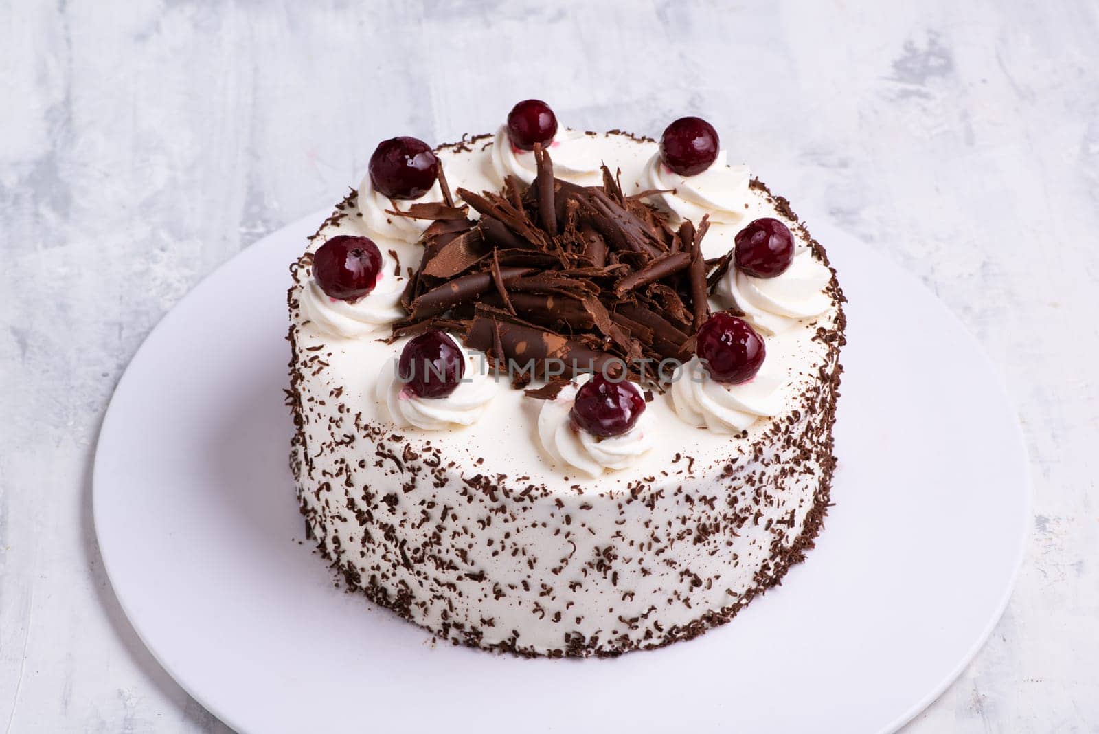 A closeup shot of white cream on Black Forest gateau cake with cherries on white marble surface