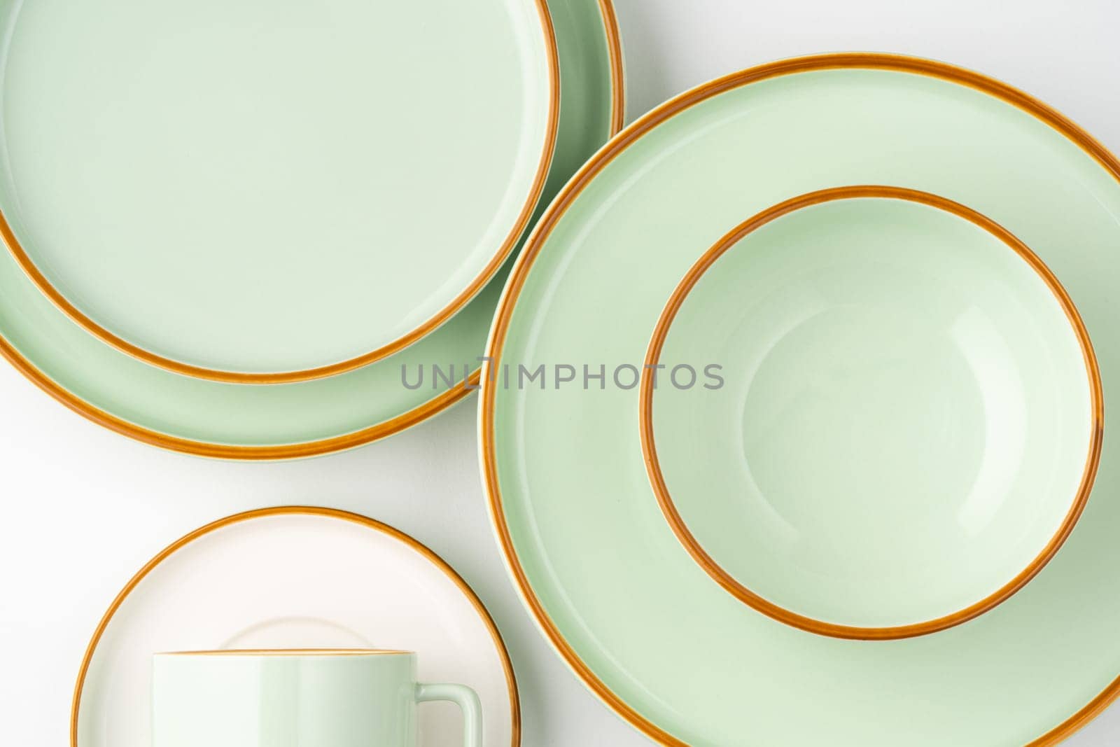A set of white and pastel green ceramic tableware with orange outlines. Top view by A_Karim