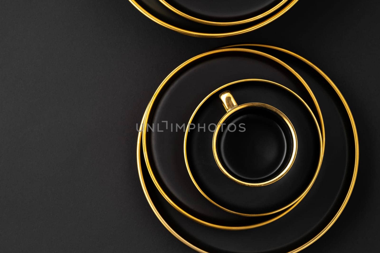 A set of black and golden ceramic plates and cup on a black background. Top view