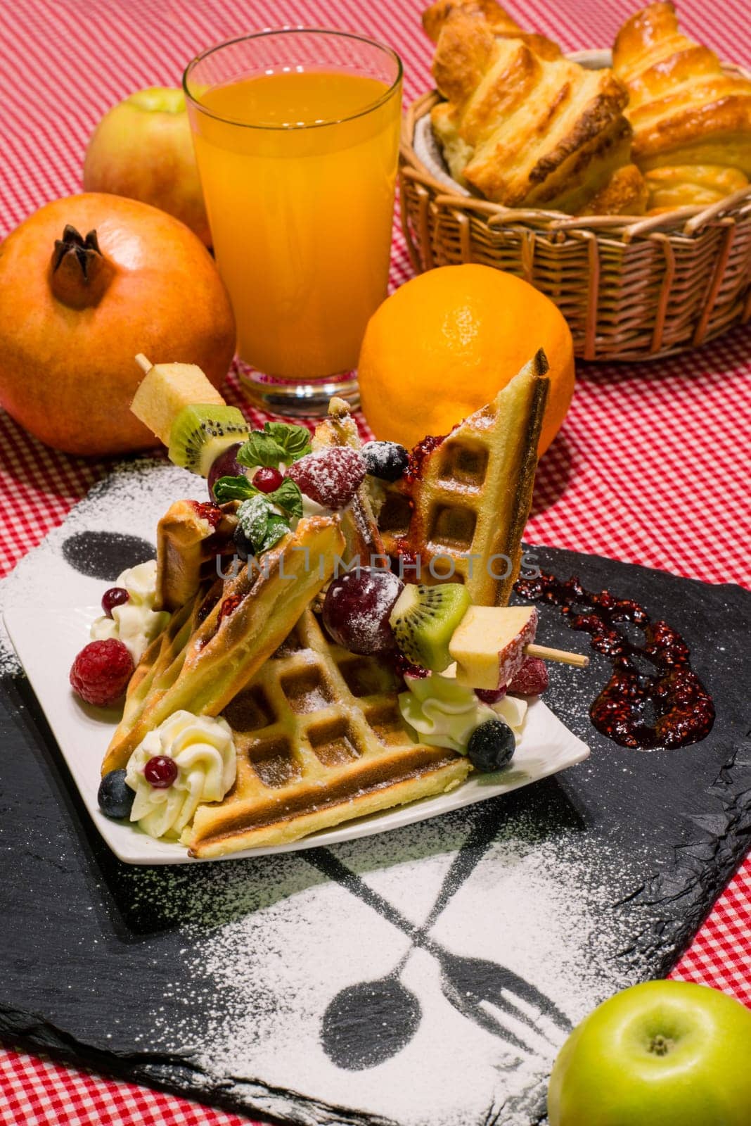Vertical closeup of delicious dessert, waffles with fruit, croissants, orange juice, served on black board by A_Karim