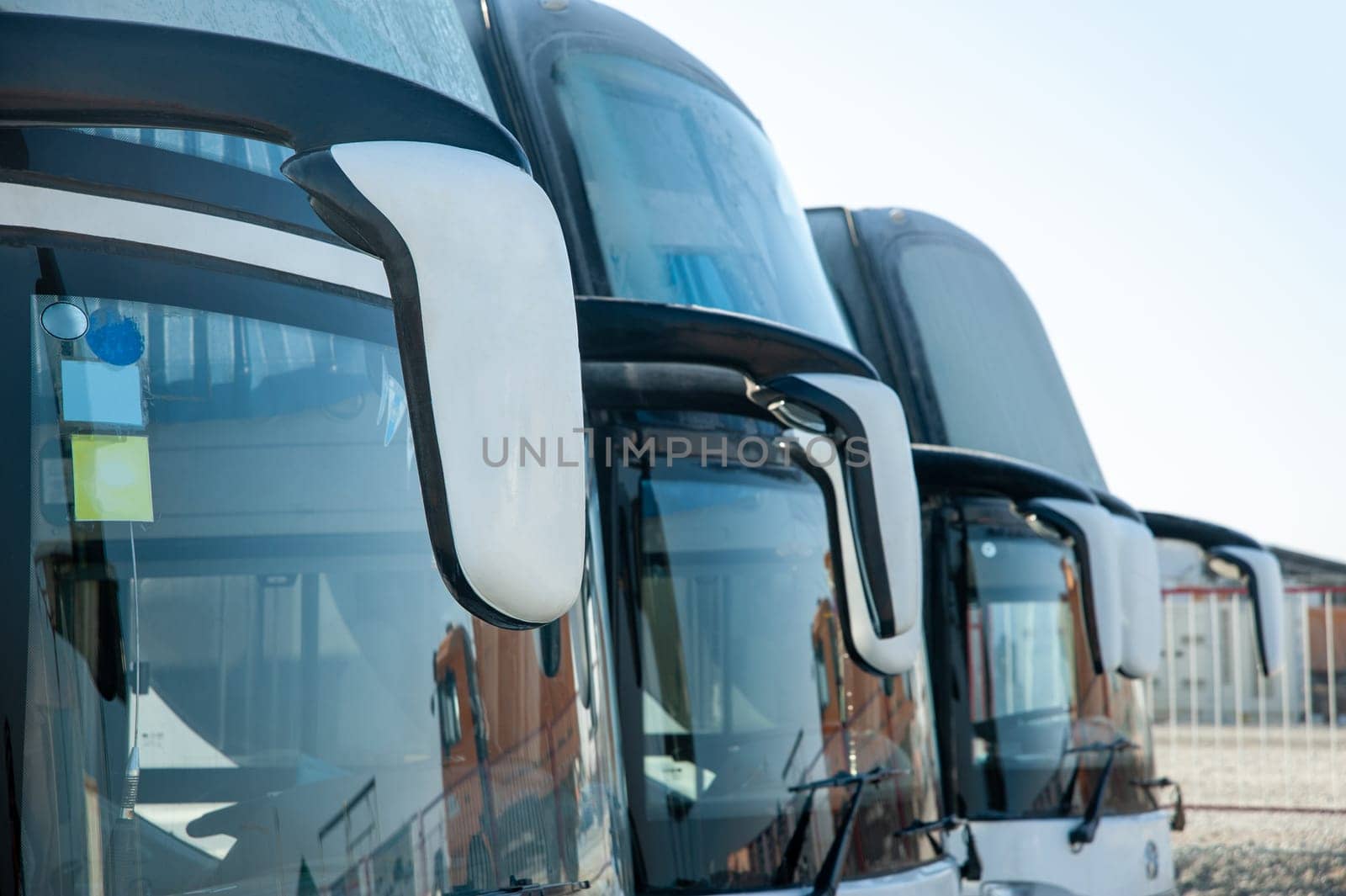 A passenger shift buses stand in a row on a construction site. Windshields