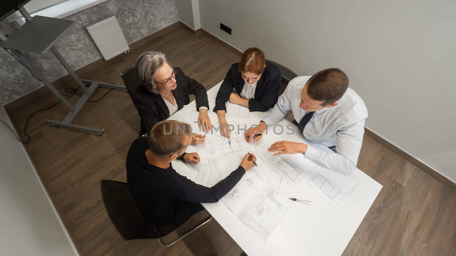 Top view of 4 business people sitting at a table and discussing blueprints. Designers engineers at a meeting. by mrwed54