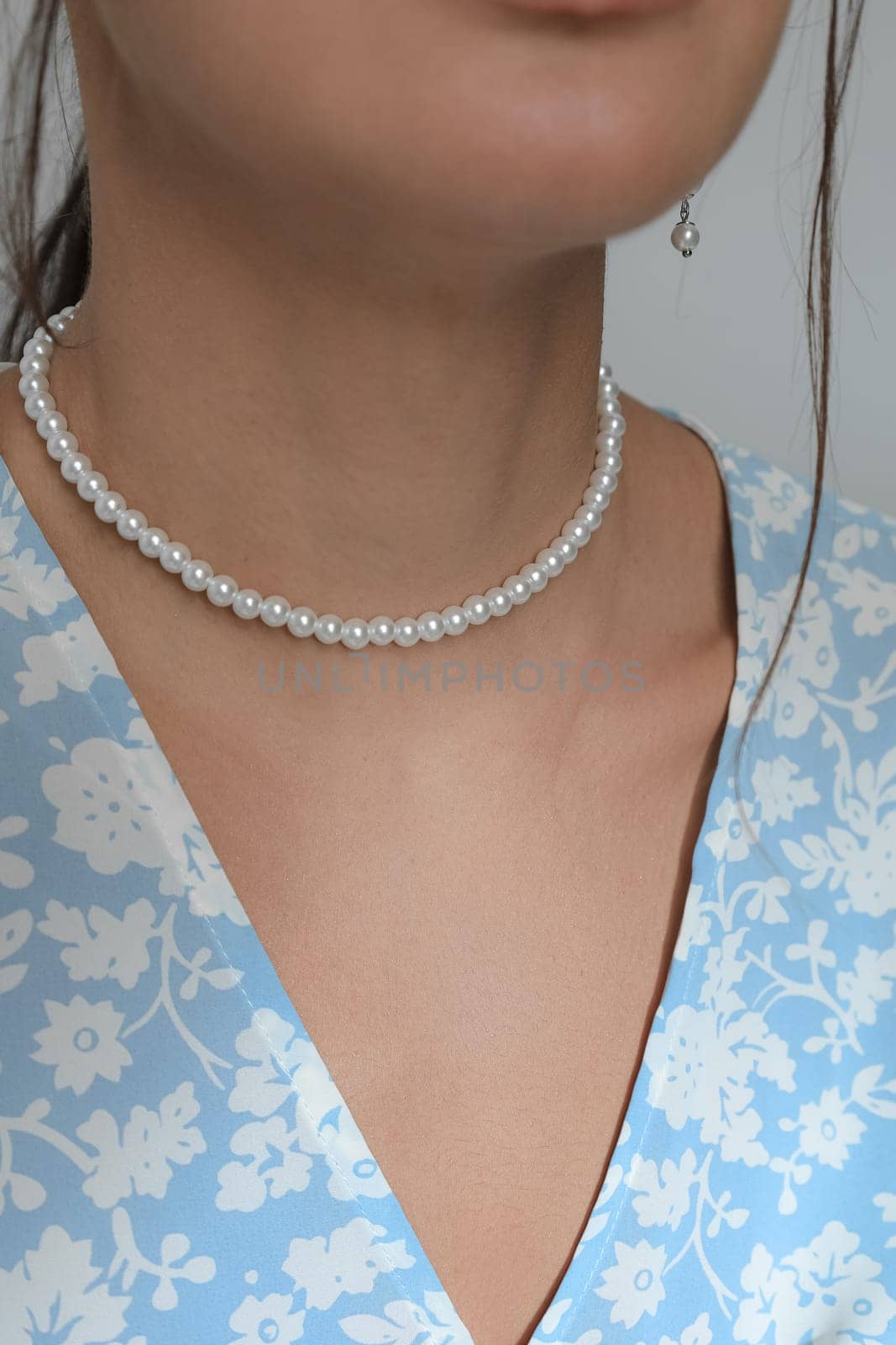 A vertical closeup of a pearl necklace around a Caucasian female's neck