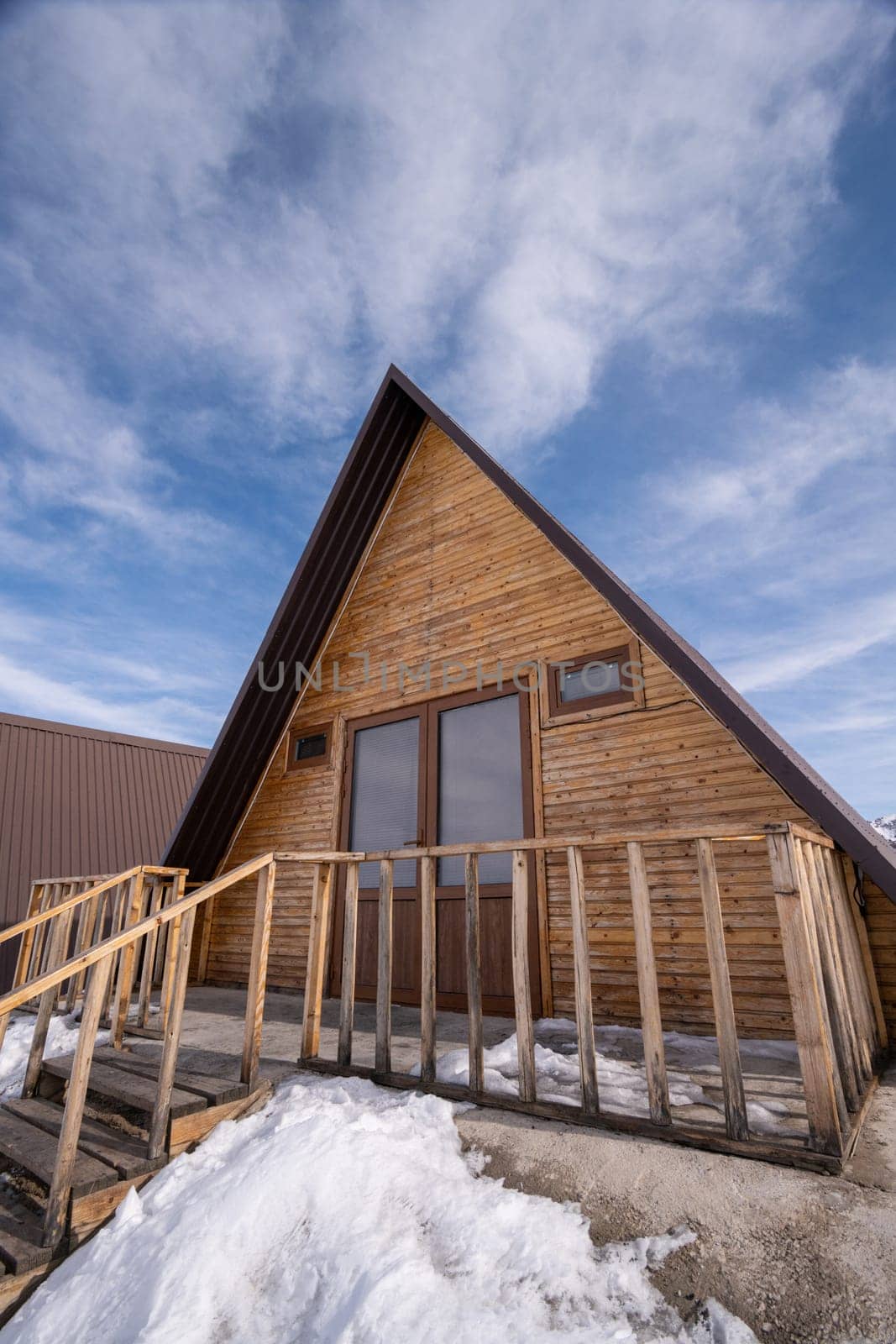 A vertical shot of a wooden cottage surrounded by snow. A recreation area in the mountains