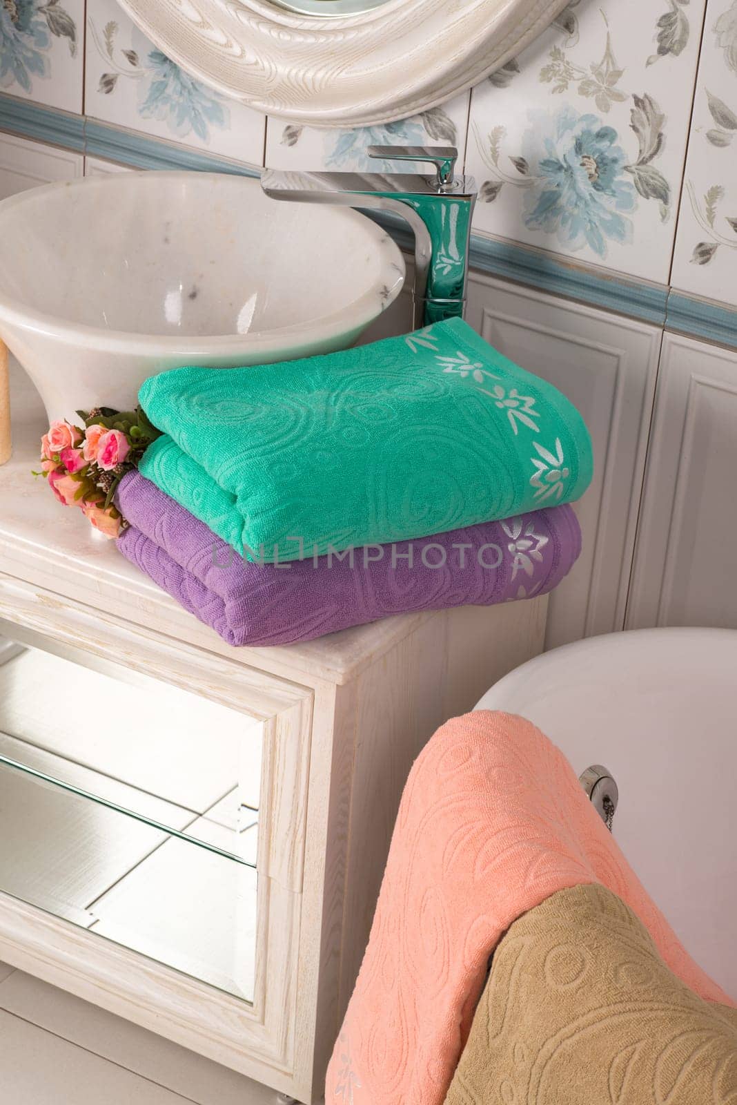 A vertical shot of folded turquoise, and purple bamboo towels and a pink towel near a bathroom sink
