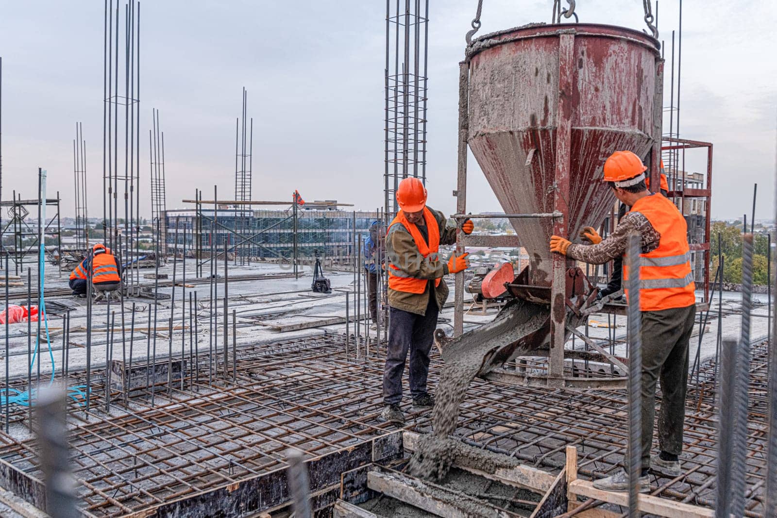 The workers on a building infrastructure roof with machinery and tools. Pouring concrete into a mold