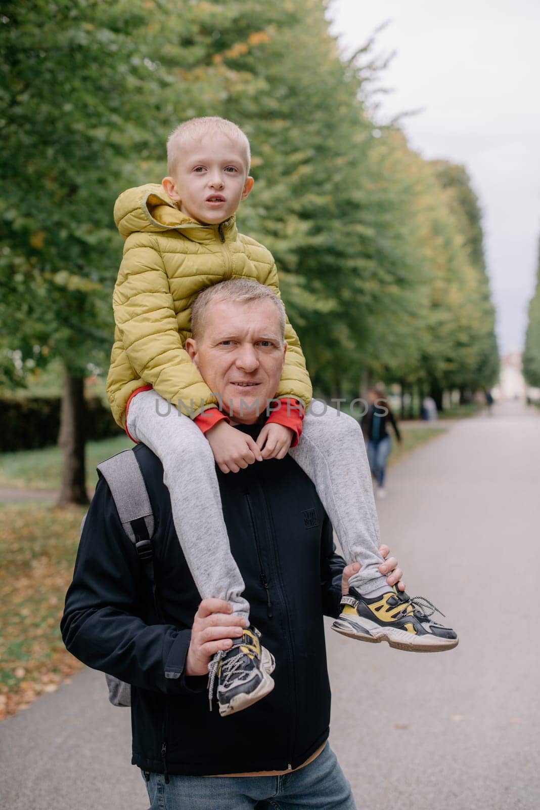 Dad holds on his son's shoulders. Beautiful family is spending time together outside. Dad and his little son are having fun on a roof terrace with view on a city. Sitting on father's shoulders and smiling.