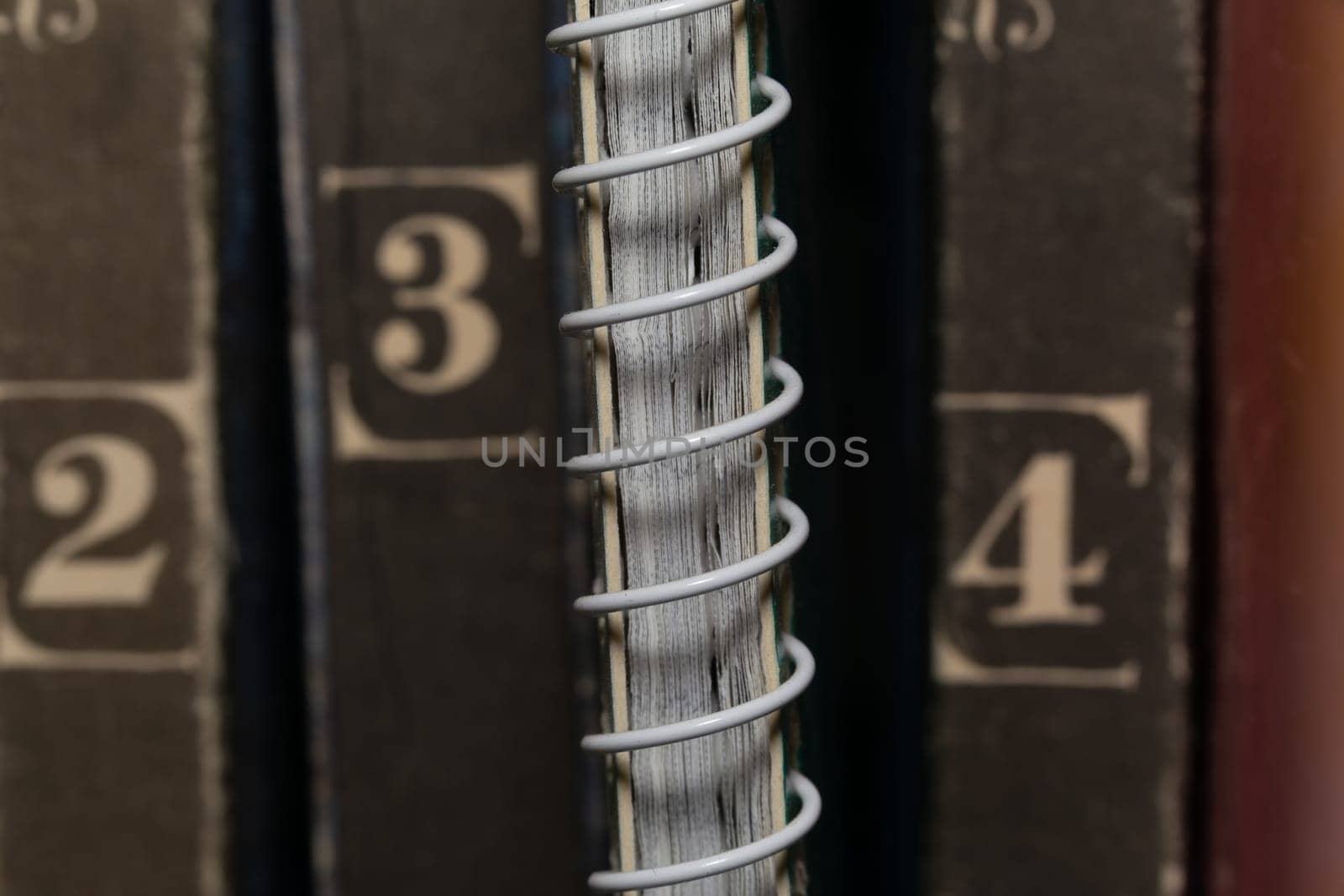 A spring-loaded notebook among old brown book volumes, close-up macro view