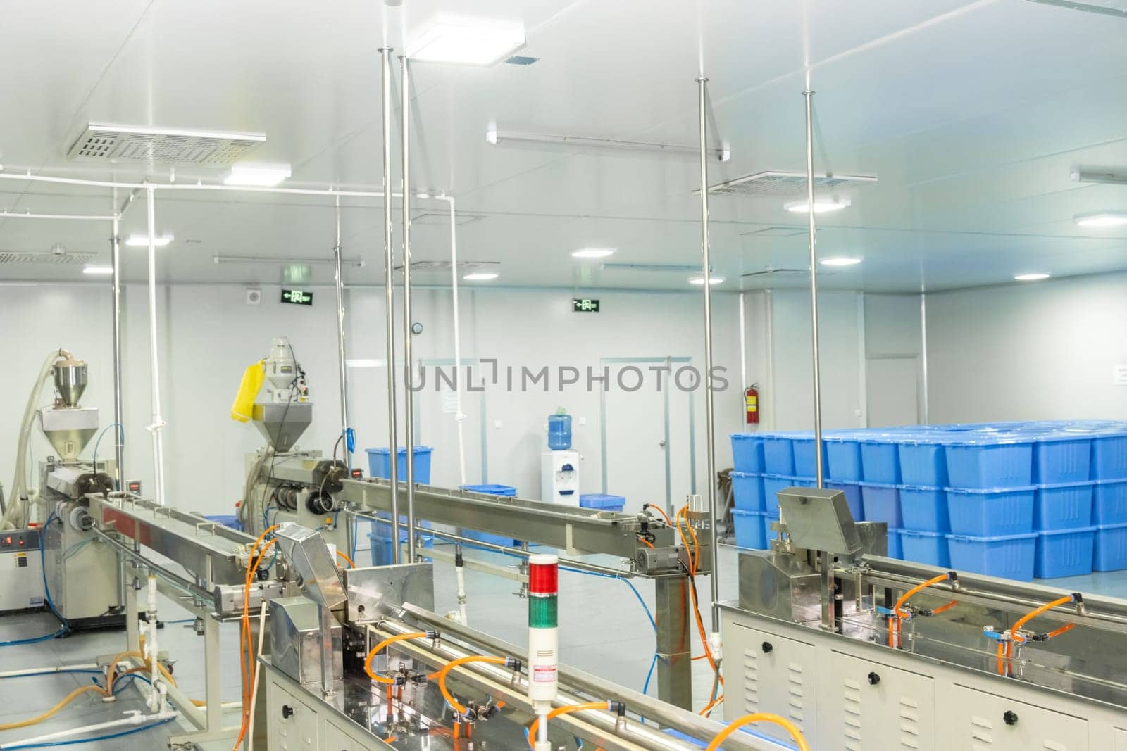 A factory of production of medical syringes and droppers, with equipment and blue containers in the background by A_Karim