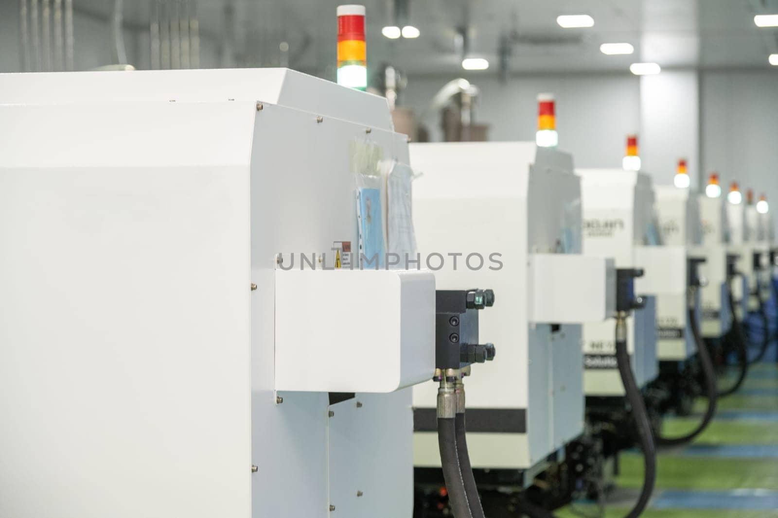 A selective focus of a molding machine from behind with hanging hosepipes in a factory for the production of medical syringes and droppers by A_Karim