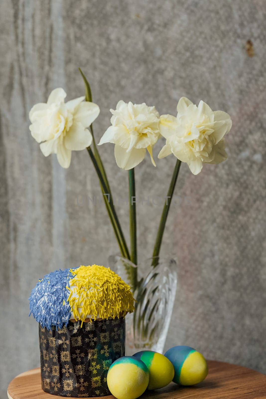 Delicious Easter cake in the colors of the flag of Ukraine, yellow-blue colored Easter eggs on a wooden table with flowers in the background. place for text. selective focus.