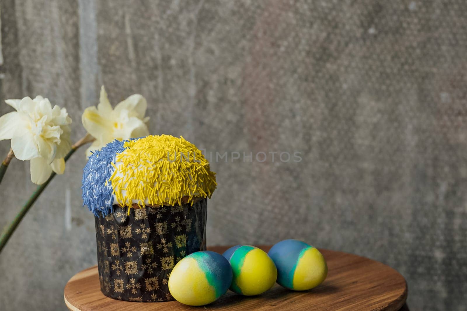 Delicious Easter cake in the colors of the flag of Ukraine, yellow-blue colored Easter eggs on a wooden table with flowers in the background. place for text. selective focus.