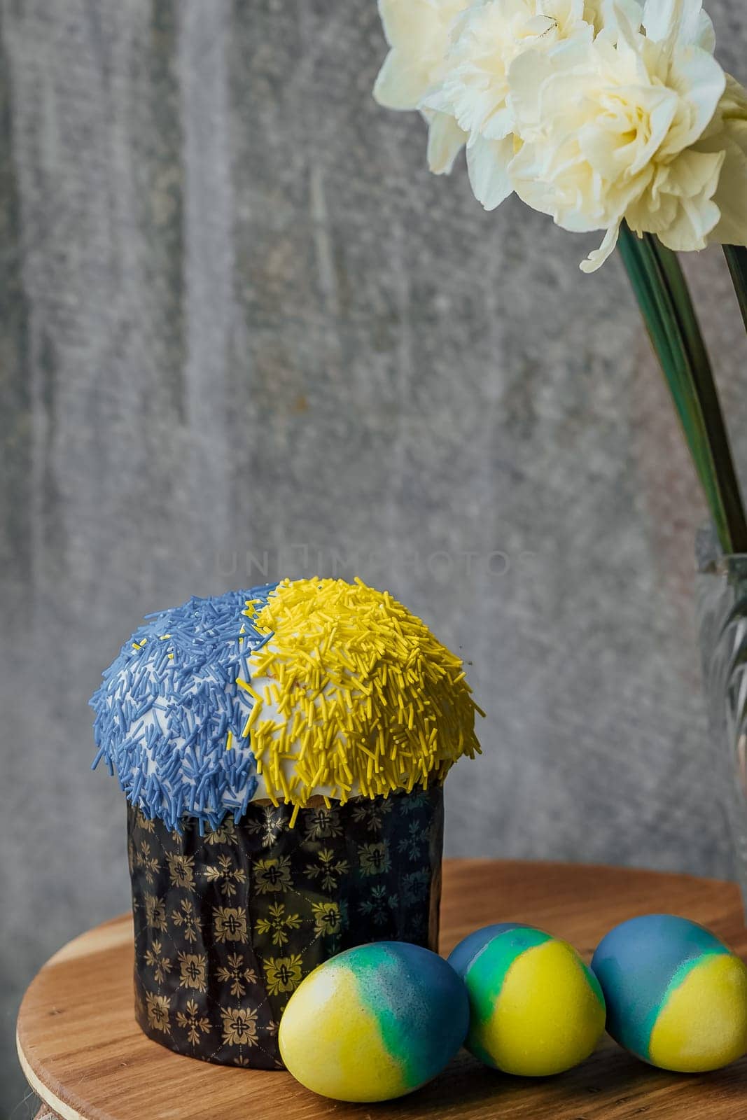 Delicious Easter cake in the colors of the flag of Ukraine, yellow-blue colored Easter eggs on a wooden table with flowers in the background. place for text. selective focus by Anyatachka