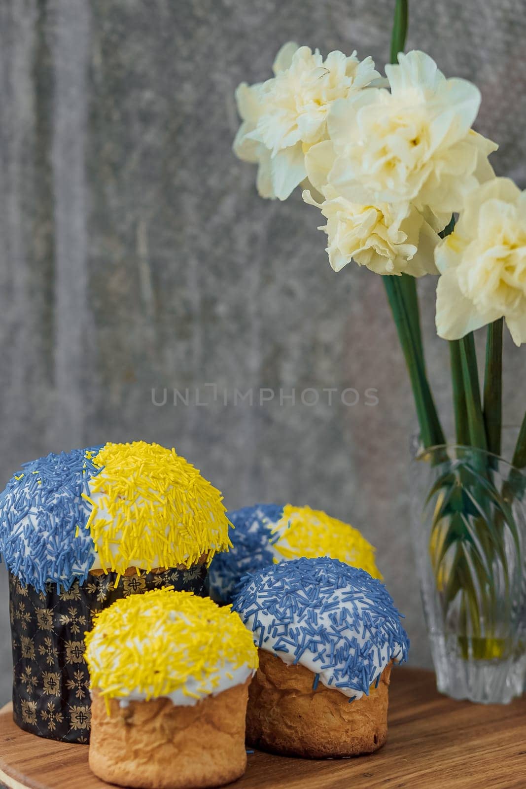 Delicious Easter cakes in the colors of the flag of Ukraine, yellow and blue on a wooden table with flowers in the background. place for text. selective focus by Anyatachka
