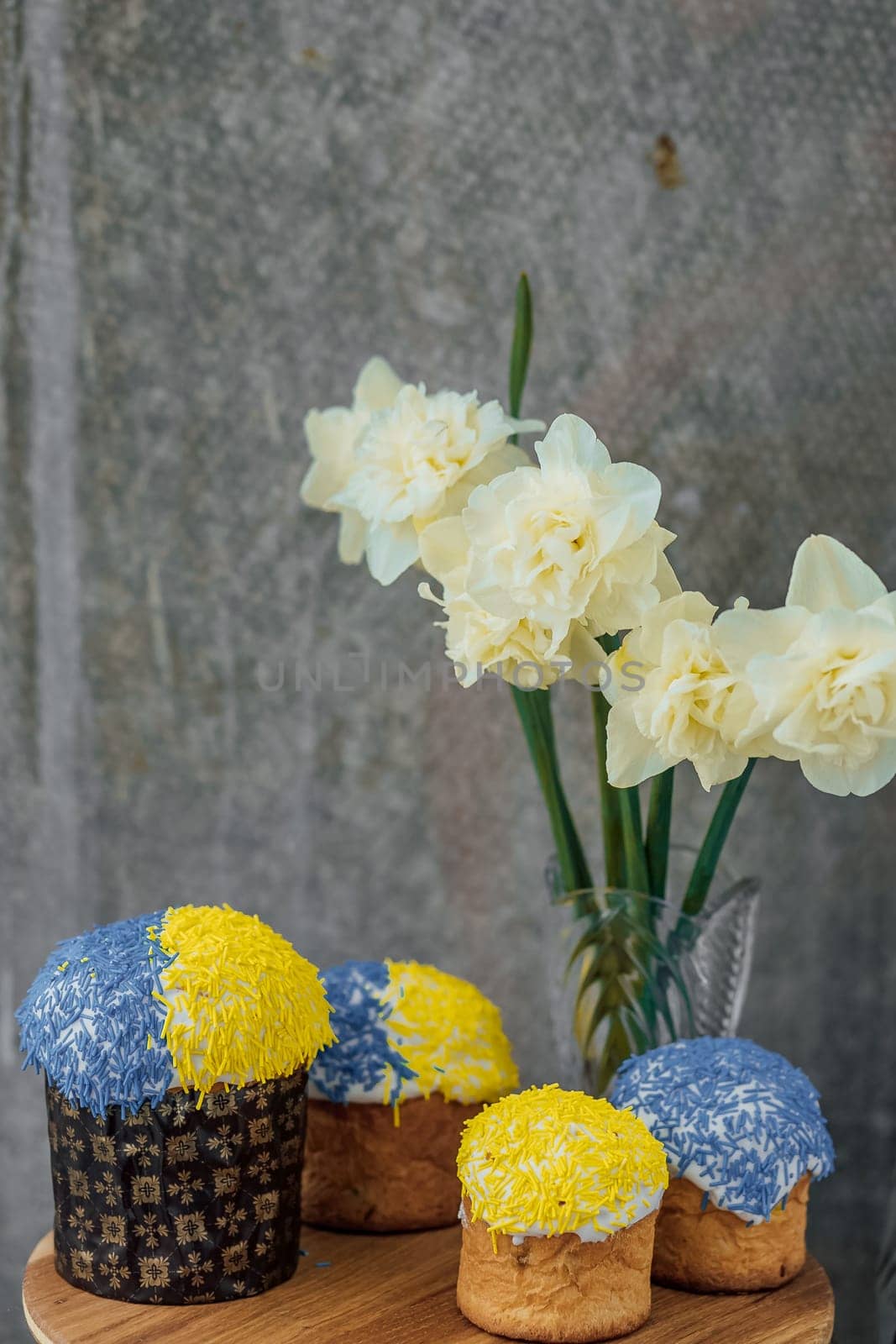 Delicious Easter cakes in the colors of the flag of Ukraine, yellow-blue colored Easter eggs on a wooden table with flowers in the background. place for text. selective focus by Anyatachka