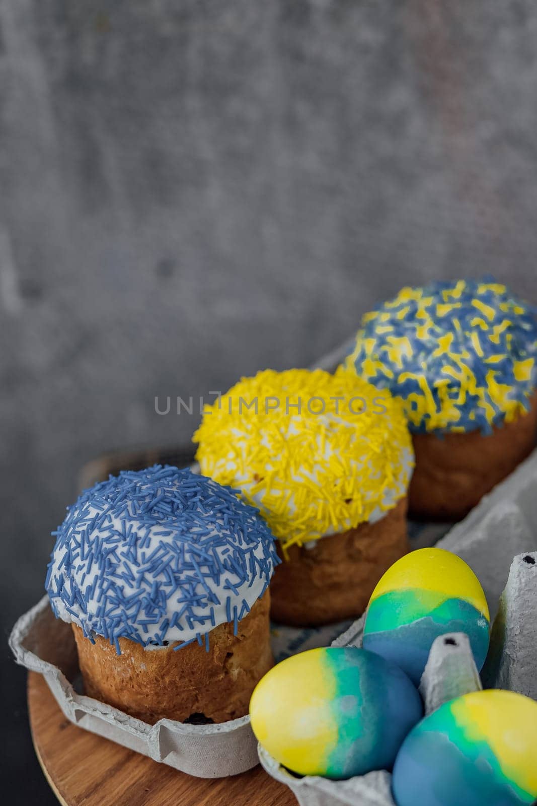 Easter cakes in the colors of the flag of Ukraine, yellow and blue in a cardboard stand with eggs, Easter eggs. place for text. selective focus by Anyatachka