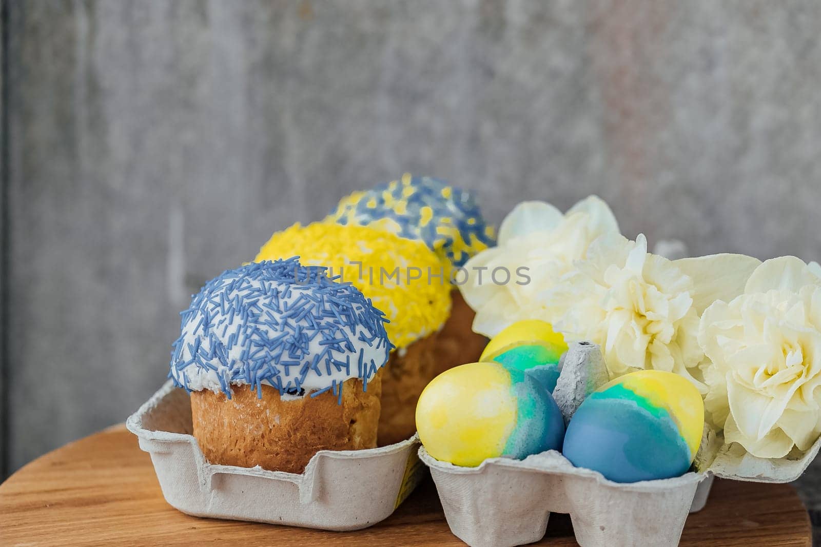 Easter cakes in the colors of the flag of Ukraine, yellow and blue in a cardboard stand with eggs, Easter eggs. place for text. selective focus.