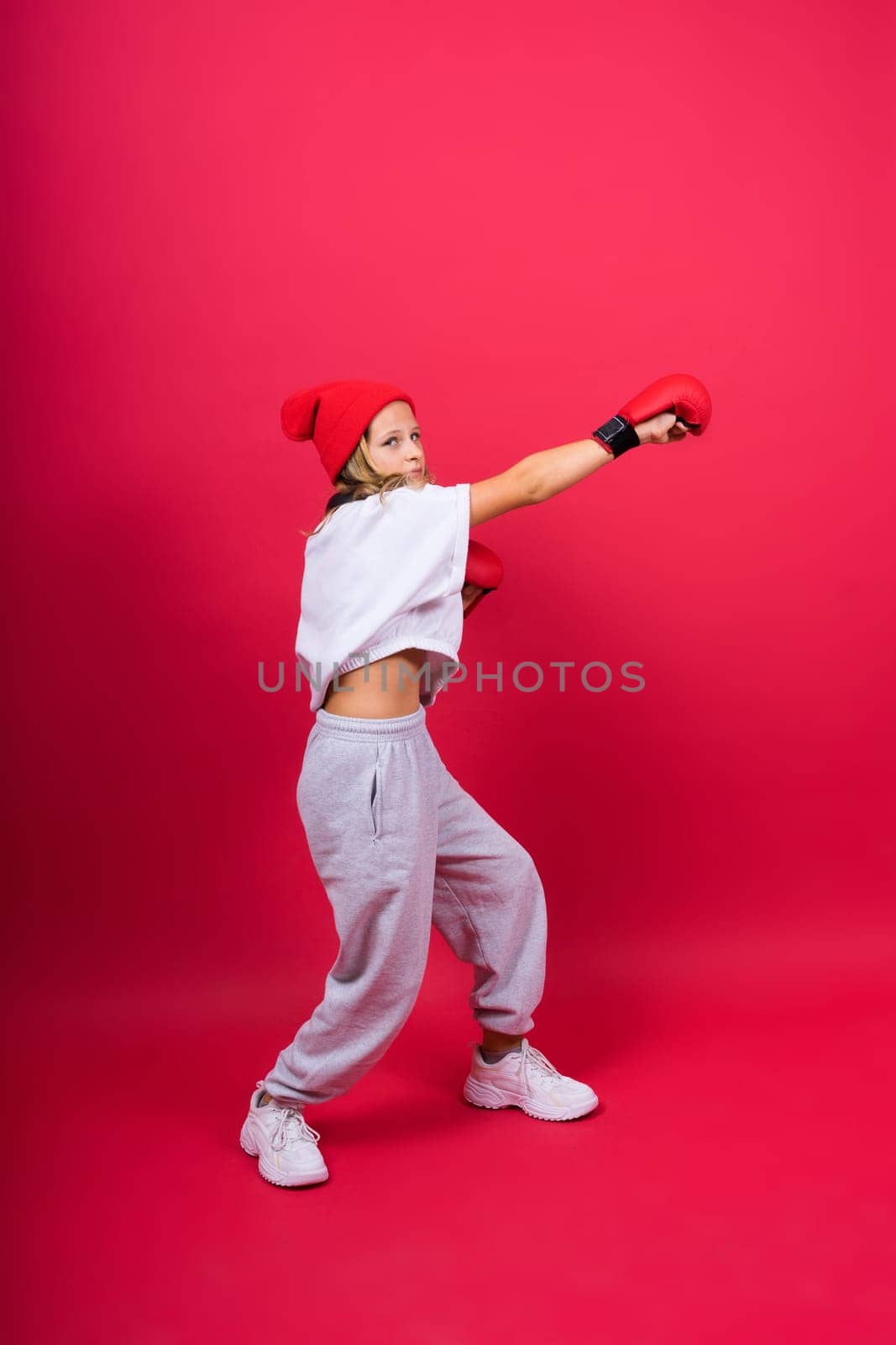 Cute little girl in boxing gloves on red background studio by Zelenin