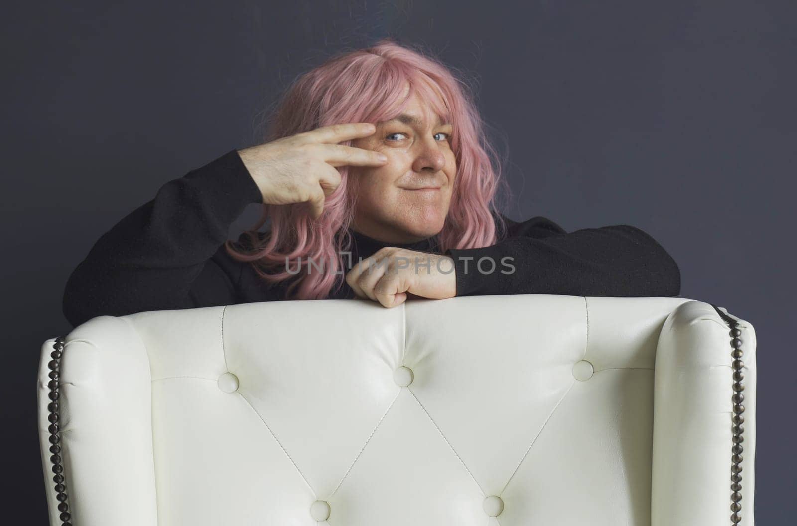 Portrait of a man in a pink wig, who makes hand movements near his eyes. Seduces, dances, entices. Close-up.